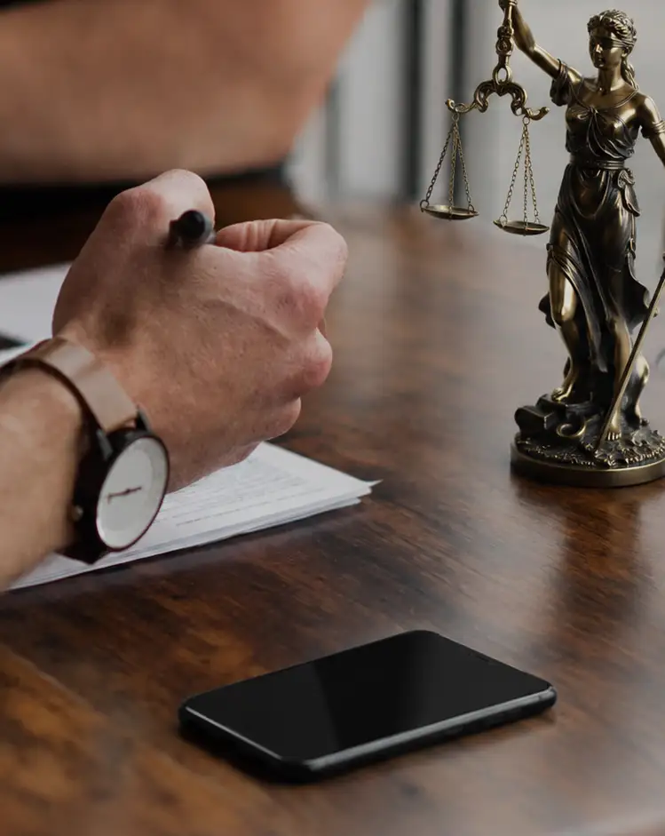Due persone a un tavolo: una prende appunti su un documento, accanto una statua della giustizia