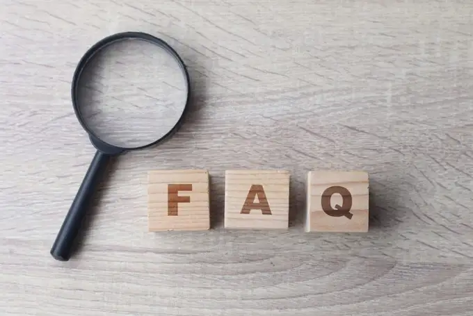 Tre cubi di legno che compongono la sigla FAQ, accanto a una lente d'ingrandimento