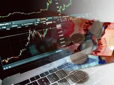 Un portatile con un grafico di mercato, banconote e monete sopra la tastiera